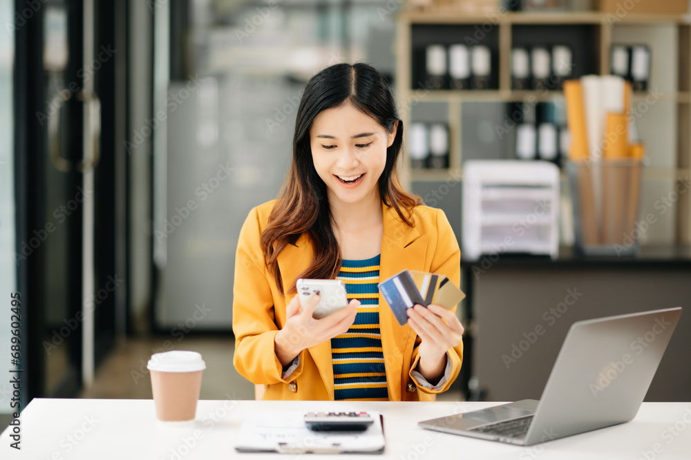 Asian Woman using smart phone for mobile payments online shopping, omni channel, sitting on table, virtual icons graphics interface screen . Asian Woman using smart phone for mobile payments online shopping, omni channel, sitting on table, virtual icons graphics interface screen .