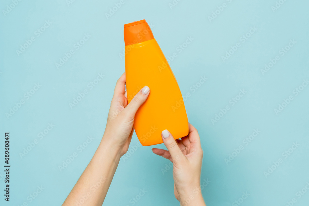 Packaging of shampoo or conditioner in woman's hand on blue background. Copy space and mock up - obrazy, fototapety, plakaty 