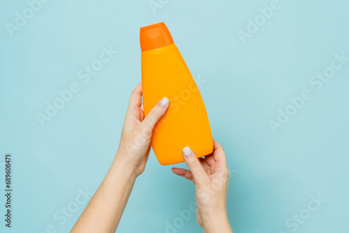 Packaging of shampoo or conditioner in woman's hand on blue background. Copy space and mock up photo