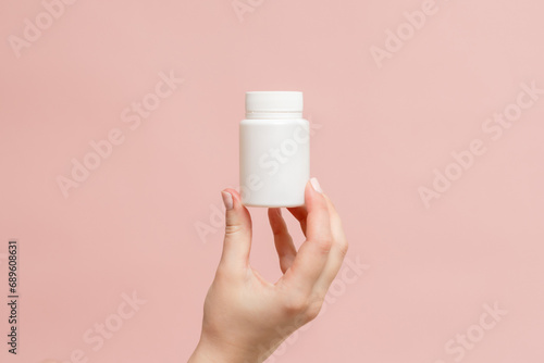 White bottle (plastic tube) in hand on pink background. Packaging for vitamins, pill or capsule, or supplement. Mockup for product branding