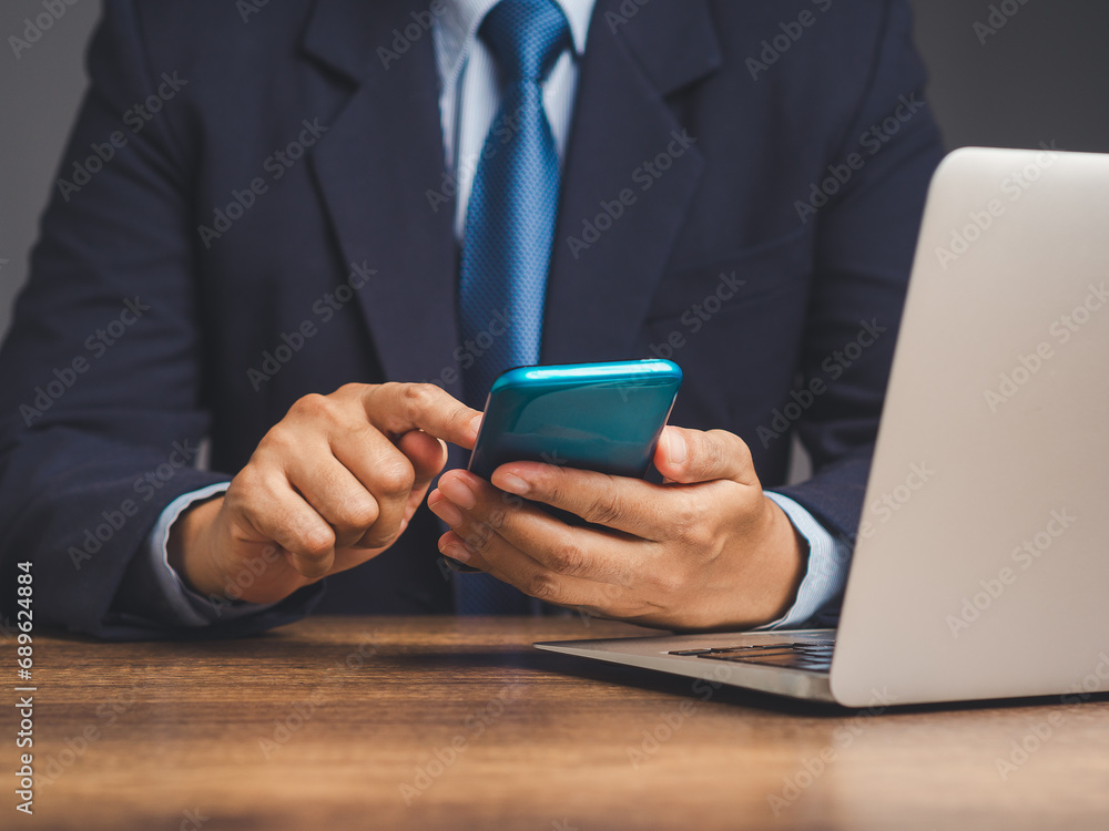 Businessman in a suit using a smartphone while sitting at a desk in the office. Businessman in a suit using a smartphone while sitting at a desk in the office.