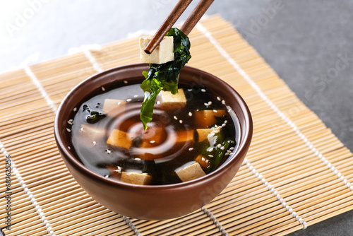 Japanese miso soup in a brown bowl. Chopsticks take tofu and wakame seaweed. photo