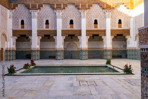 Interior of the main courtyard of the Ben Youssef Madrasa. Fountain in the middle of the patio. Walls full of tiles. Sunny day.