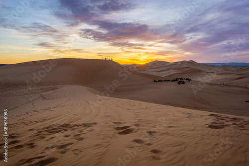 Sunset in the dunes of the Sahara desert. Camels sitting in the dunes. Sunset with some cloud and many colors