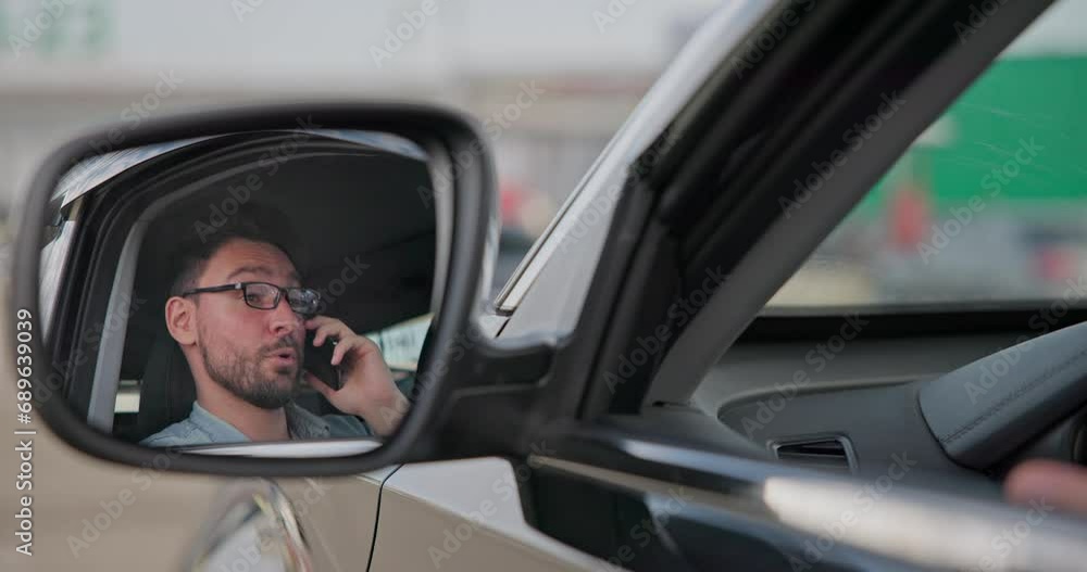 Car Side view mirror reflection - Young man sits in a car on a parking lot and talking on the phone Car Side view mirror reflection - Young man sits in a car on a parking lot and talking on the phone