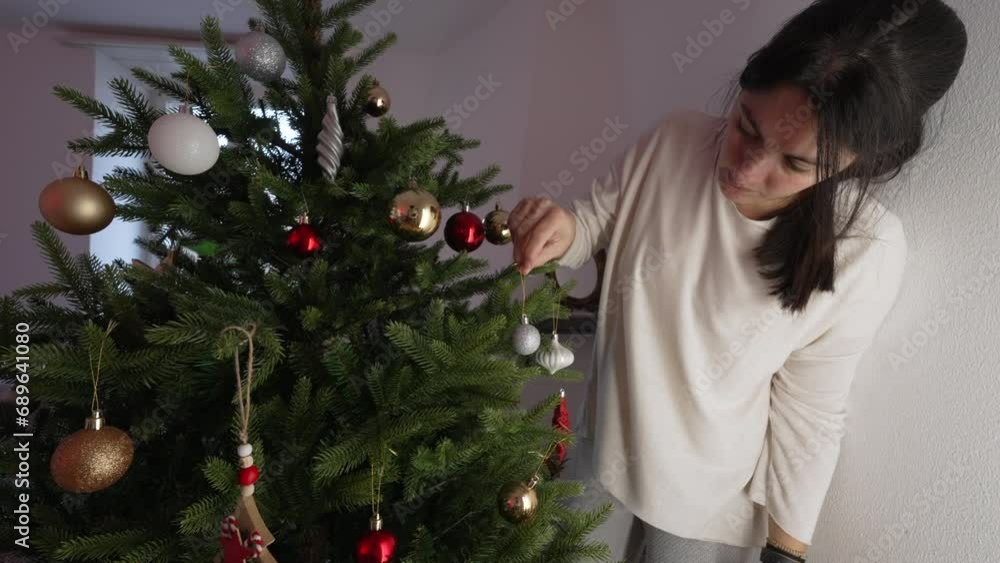 Woman decorating Christmas tree during holiday season. Person adding ornament balls, preparing for festivities Woman decorating Christmas tree during holiday season. Person adding ornament balls, preparing for festivities
