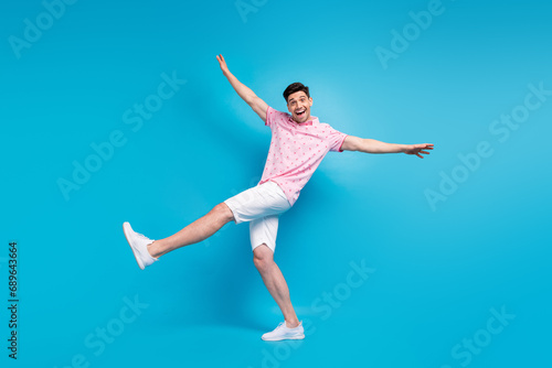 Full size portrait of cheerful overjoyed young man good mood raise arms dancing isolated on blue color background