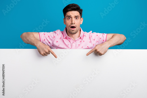 Portrait of impressed speechless man open mouth direct fingers empty space banner isolated on blue color background