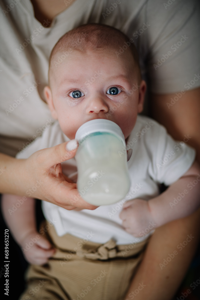 Baby enjoying nutritious meal. Mother feeding baby. Nanny formula feeding little child as alternative to breastfeeding. Baby boy or girl lying on couch and drinking milk from plastic bottle Baby enjoying nutritious meal. Mother feeding baby. Nanny formula feeding little child as alternative to breastfeeding. Baby boy or girl lying on couch and drinking milk from plastic bottle