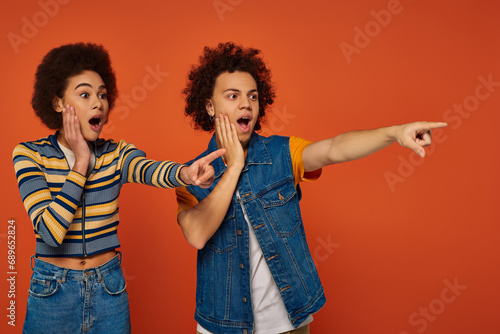 shocked african american siblings in casual attires pointing somewhere together, family concept