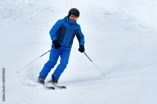 A man in blue sportswear on skis rides down a snowy slope