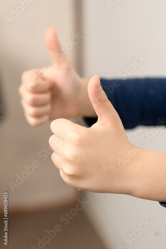 Child's hands gesturing thumbs up, a universal sign of approval and positivity, creating a moment of "OK" against a neutral background