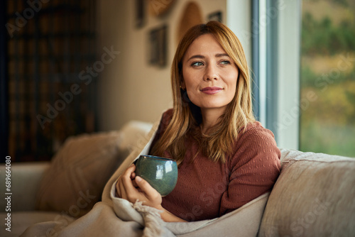 A pretty lady, looking through the window, enjoying the view with a cup of coffee.