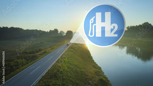 Hydrogen powered car drives into the sunset on an idyllic road at edge of river. H2 Sybol Concept of modern, green, clean fuel type photo