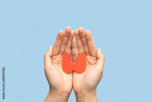 World Thyroid Day concept. Human hand holding thyroid gland shape made from paper on blue background. Awareness of thyroid disease such as hyperthyroidism, hypothyroidism and thyroiditis. photo