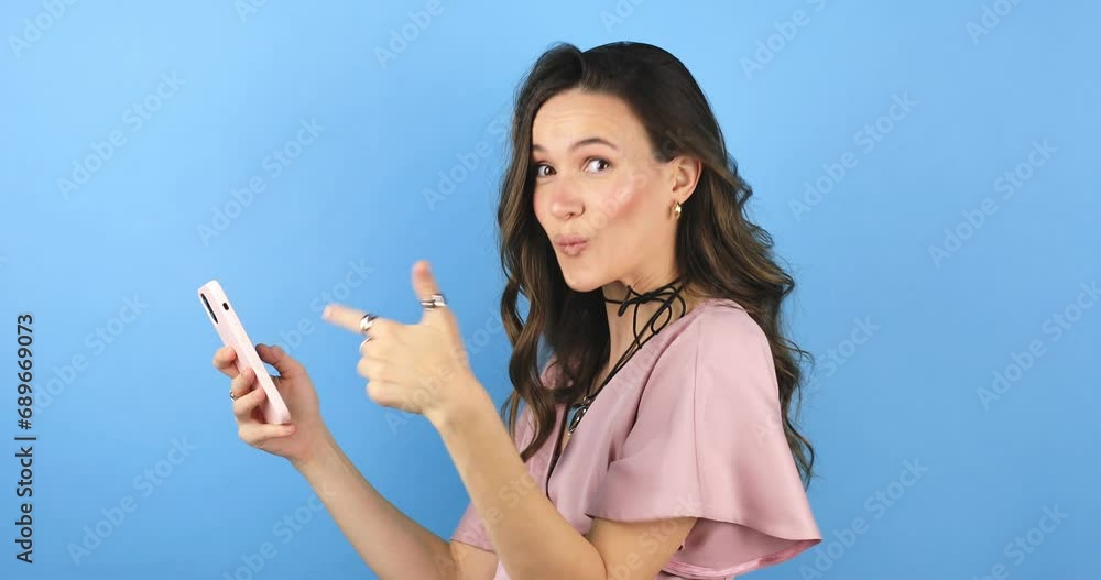 Attractive brunette woman look surprised wow hold using mobile cell phone on blue background. Girl look on smartphone and doing winner gesture. Girl just found out big win news, point on phone, wow. Attractive brunette woman look surprised wow hold using mobile cell phone on blue background. Girl look on smartphone and doing winner gesture. Girl just found out big win news, point on phone, wow.