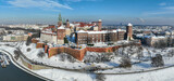 Krakow, Poland. Royal Wawel Cathedral and castle covered with snow in winter. Vistula river and tourist boats. Aerial panorama with boulevard, promenades and walking people. Old city in the background