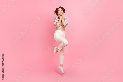 Full size photo of gorgeous adorable cute girl dressed stylish blouse flying hold arms on cheekbones isolated on pink color background