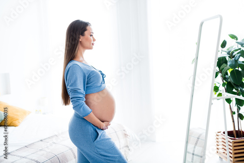 Photo of adorable lovely cute girl waking up dressed in pajamas looking her belly waiting for baby white light indoors