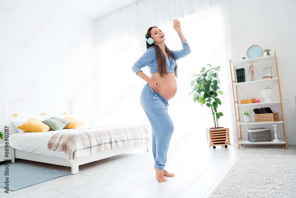 Photo of positive glad cute adorable pregnant girl listen music dance enjoy carefree time in flat white light room interior indoors Photo of positive glad cute adorable pregnant girl listen music dance enjoy carefree time in flat white light room interior indoors