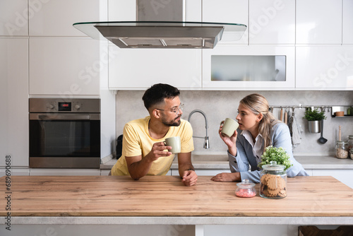 Small talks. Man and woman standing in the kitchen chitchatting while they drinking coffee after female come back home from her workplace. Businesswoman and her roommate relaxing afternoon photo