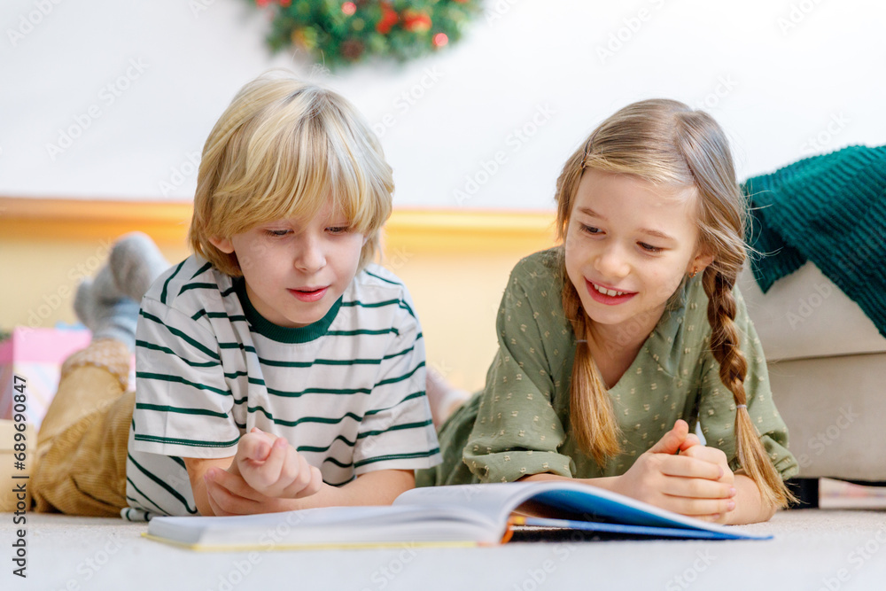boy and girl have fun near christmas tree, lay on floor reading a book, smiling and laughing boy and girl have fun near christmas tree, lay on floor reading a book, smiling and laughing