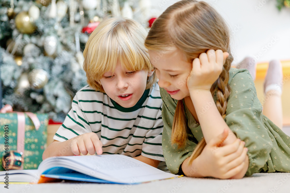 boy and girl have fun near christmas tree, lay on floor reading a book, smiling and laughing boy and girl have fun near christmas tree, lay on floor reading a book, smiling and laughing
