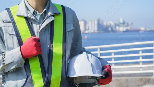 ヘルメットと作業服の男性・海と工業地帯│建設業・製造業・プラント イメージ
