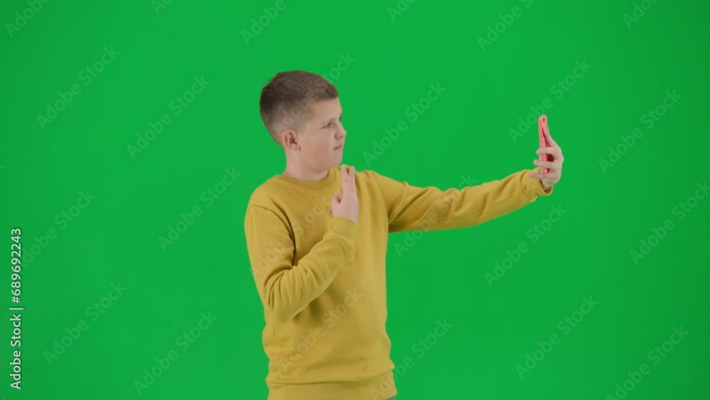 Portrait of boy on chroma key green screen. Schoolboy in casual taking selfie on smartphone, cool pose smiling face expression. Middle shot. Portrait of boy on chroma key green screen. Schoolboy in casual taking selfie on smartphone, cool pose smiling face expression. Middle shot.