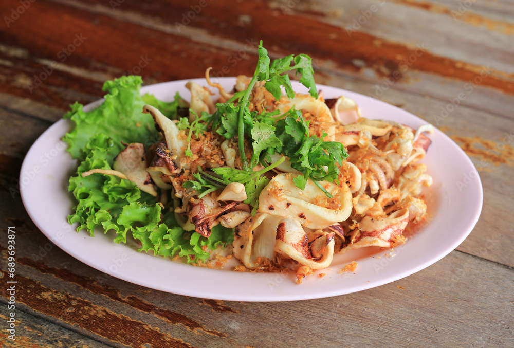 Fried Squid with crispy garlic in plate on wood table. Thai style food.