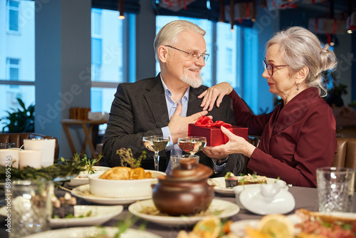 Mature couple celebrating New Year man giving present box to woman