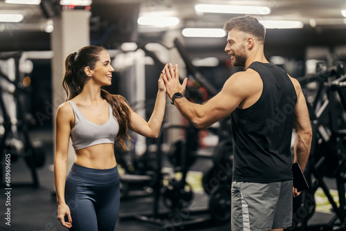 A fitness trainer is giving high five to a sportswoman in a gym.
