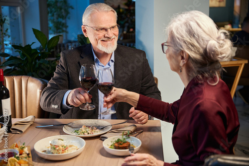 Joyful aged man and woman clinking glasses of wine during Christmas celebration