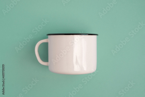 White blank vintage enamel mug isolated on green color studio background. Retro style steel cup, empty mock-up. Banner. Copy space. Place for logo, text, advertising. Tourism, hiking, journey photo