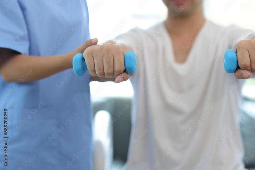 Nurse in an examination room at a hospital is doing physiotherapy for a male patient's arm with dumbbells lifting up and down. Nurse in an examination room at a hospital is doing physiotherapy for a male patient's arm with dumbbells lifting up and down.