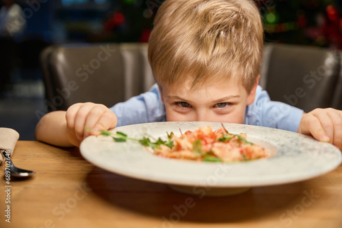 Funny little boy looking at plate with festive dish while celebrating New Year