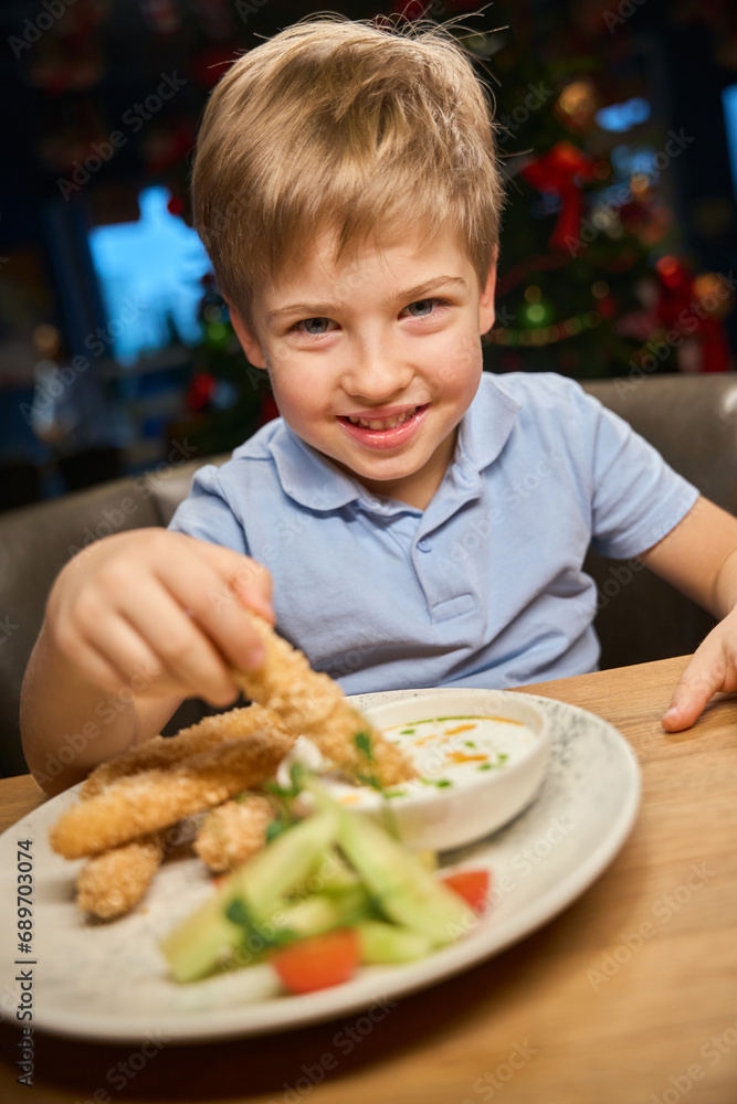 Cheerful little boy eating French fries with nuggets during New Year celebration Cheerful little boy eating French fries with nuggets during New Year celebration