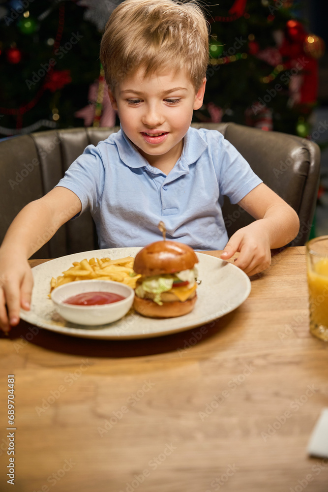 Little boy looking at big burger on his plate in restaurant on Christmas dinner Little boy looking at big burger on his plate in restaurant on Christmas dinner