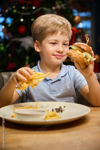 Joyful little boy enjoying tasty sandwich at festive dinner on Christmas