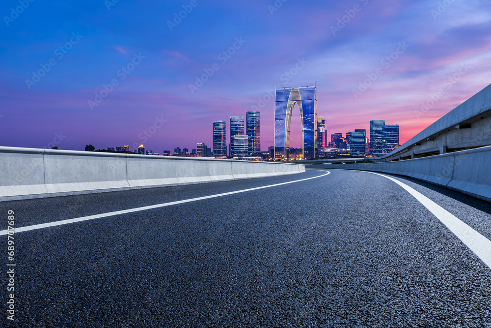 Asphalt road and city skyline with modern building at night in Suzhou, China. Road and city buildings background.