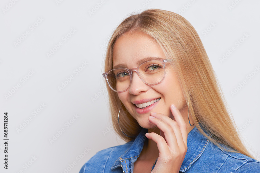 Fair-haired girl closeup wears blue denim shirt and glasses holds one hand at her face and smiles, good mood concept, copy space