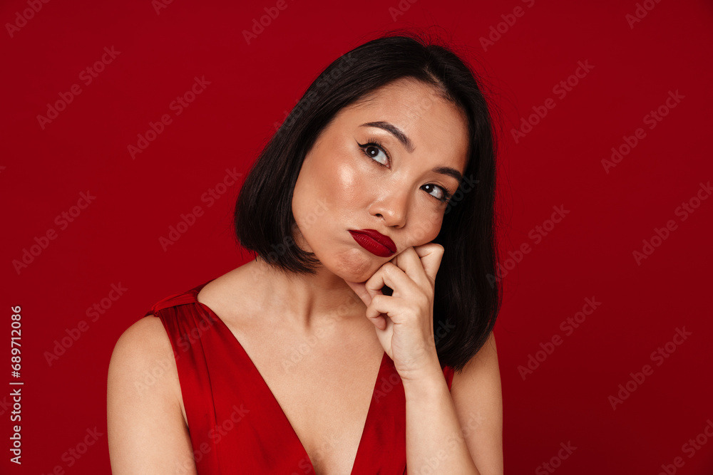 Upset asian woman looking away while standing isolated over red wall Upset asian woman looking away while standing isolated over red wall