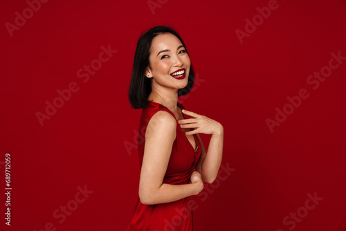 Lovely asian woman smiling and looking away while posing isolated over red background