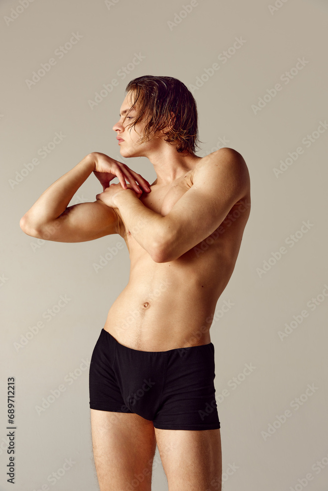 Handsome young man with fir, sportive muscular body posing in underwear shirtless against grey studio background. Concept of men's beauty, health, body care, sportive lifestyle Handsome young man with fir, sportive muscular body posing in underwear shirtless against grey studio background. Concept of men's beauty, health, body care, sportive lifestyle