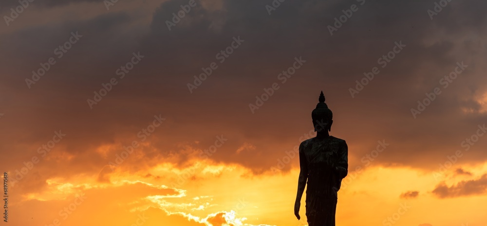 Stand big Buddha Statue in silhouette sun set Light background in park of Thailand temple.Yellow orange light silhouette dark shadow of image Buddha statue stand Buddha tall walk in sun light cloud. Stand big Buddha Statue in silhouette sun set Light background in park of Thailand temple.Yellow orange light silhouette dark shadow of image Buddha statue stand Buddha tall walk in sun light cloud.