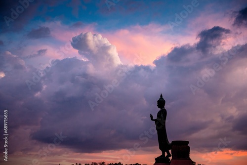 Stand big Buddha Statue in silhouette sun set Light background in park of Thailand temple.Yellow orange light silhouette dark shadow of image Buddha statue stand Buddha tall walk in sun light cloud. © BESTIMAGE
