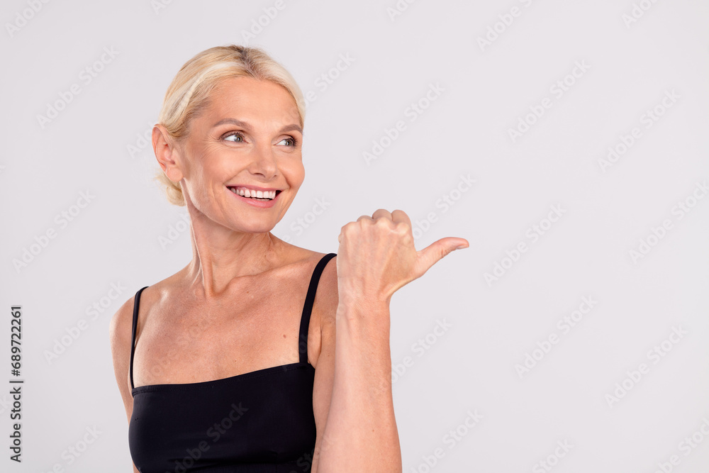 Portrait of beautiful pensioner woman face care advertisement directing finger empty space cosmetology isolated on gray color background Portrait of beautiful pensioner woman face care advertisement directing finger empty space cosmetology isolated on gray color background