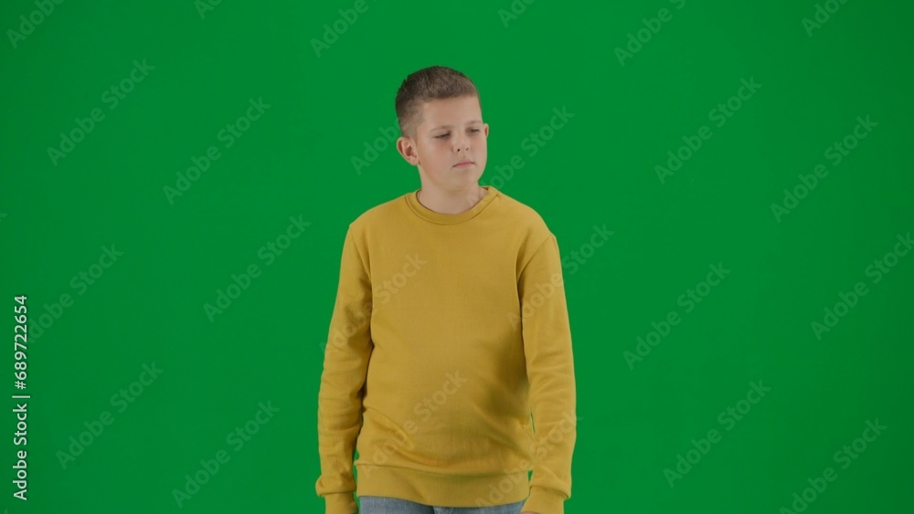 Portrait of kid boy on chroma key green screen. Schoolboy in jeans walking at the camera looking around. Middle body front shot. Portrait of kid boy on chroma key green screen. Schoolboy in jeans walking at the camera looking around. Middle body front shot.