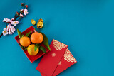Chinese New Year. Red packet envelope, flowers, mandarins, festival decorations on teal color background. Flat lay, top view.