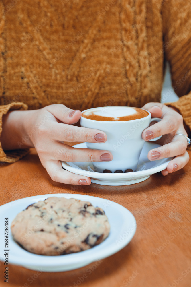vertical image of unrecognizable woman in cafeteria with cup of coffee and cookie on table